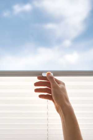 cropped shot of female hand pull up and close cordless shades on window in bedroom, controlling lighting range, protection of daylight, blue sky view, modern accessoriesの写真素材