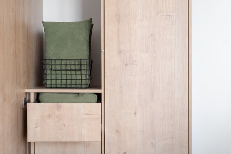 closeup of pillows folded in metal basket inside wooden wardrobe with open door and drawers in living room with modern interior, storage conceptの写真素材