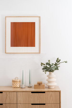 detail in bedroom with elegant interior, wood chest of drawers, candlesticks, ceramic vase with eucalyptus branches, jewelry box and frame picture on wallの写真素材