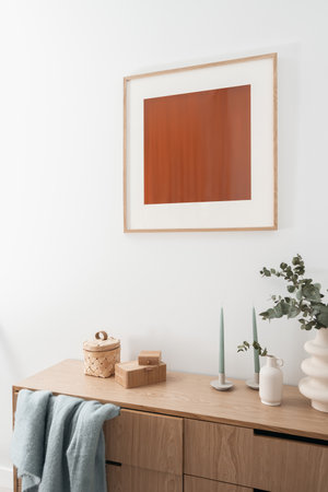 detail in living room with stylish interior, wall decor, eucalyptus branches, candlestick and bamboo jewelry box on wooden chest of drawersの写真素材