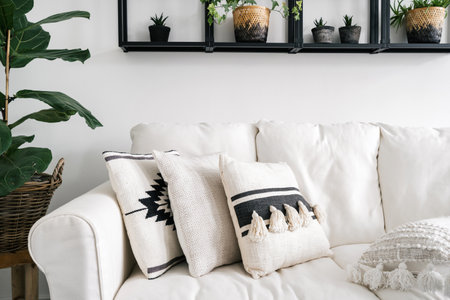 comfort couch with cushions in linen covers, plant in pots on metal shelf on wall in living room with ethnic boho interior at stylish apartmentの写真素材