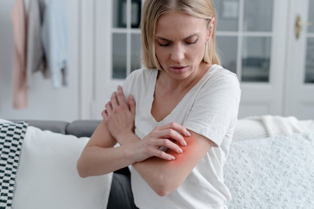 worried female feeling unwell, has allergy or reaction from insect bite, girl with itch or irritation on arm sitting on sofa in roomの写真素材