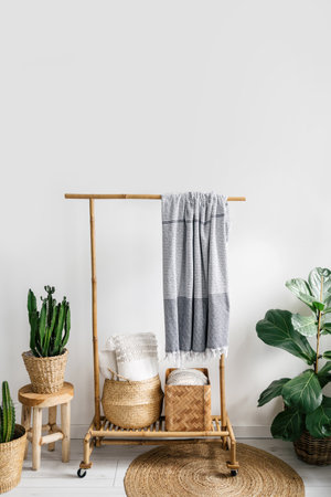 detail in room with boho interior, plaid hanging on wooden clothes rack, pillows inside wicker basket, potted plants and round rug on floor, storage conceptの写真素材