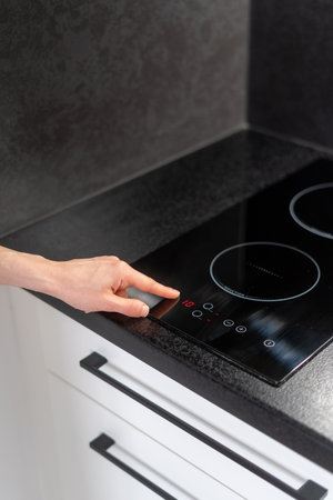 cropped shot of female hand press button on glass ceramic induction hob and select temperature mode on control panel, modern household appliances conceptの写真素材