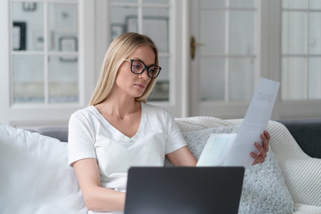 thoughtful female wearing glasses reading document, concentrated girl remote employee engaged in studying terms conditions of loan agreement by homeの写真素材
