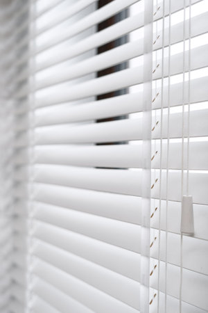 Concept of modern window blinds for sunlight protection in the room. Selective focus of wooden jalousie with horizontal slats on plastic window. Advertising of apartment decor with natural materialの写真素材