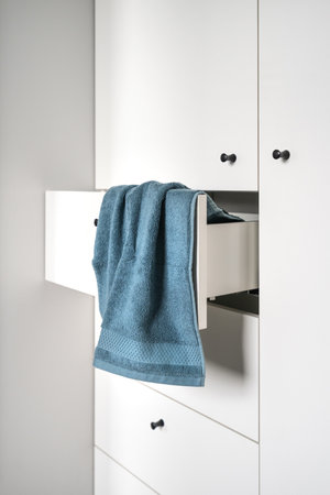 closeup of blue terry towel hanging on open drawer of white wooden wardrobe, modern furniture in nordic style at apartmentの写真素材
