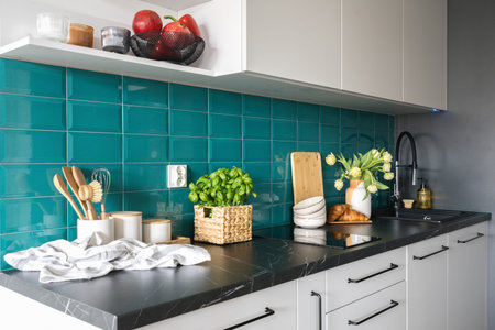 cozy kitchen with white furniture and blue tile on wall, ceramic vase with flowers, croissants on...