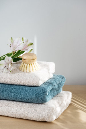 Folded, clean soft towels, small bamboo brush and flower on the wooden beige table. Daylight and shadows in bathroom. Hygiene conceptの写真素材