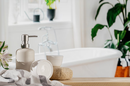Close up view of skincare and bodycare products. Ceramic soap dispenser bottle, jars with moisturizing cream, bath sponge and fresh towel on the wooden table against blurred bathroom backgroundの写真素材