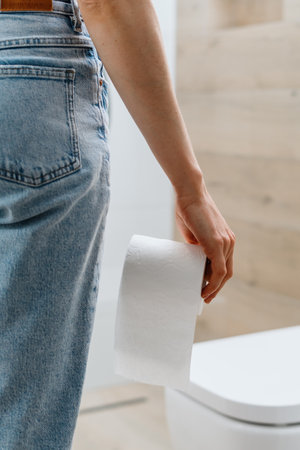 Vertical shot of a woman standing in the restroom and holding a roll of white toilet paper. Concept of intestinal problems and diarrheaの写真素材