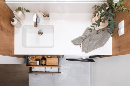 interior in small domestic washroom, washbasin with chrome mixer, vase with eucalyptus branch on countertop and open drawer of under sink cabinet with clean towels and body care productsの写真素材