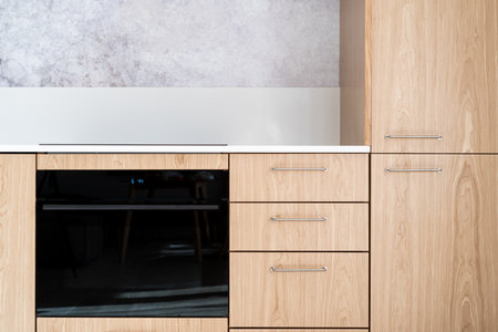 Front view of kitchen module with wooden facade and new black integrated oven with microwave mode. Concepts of household appliance in modern apartmentの写真素材