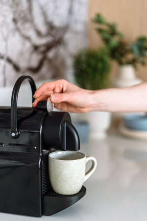 Cropped view of woman hand putting espresso capsule to coffee machine with empty cup. Preparing...