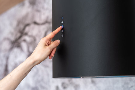 Cropped view of woman hand select mode on black modern cooking hood with illuminated buttons, standing near kitchen appliance in contemporary interior.の写真素材