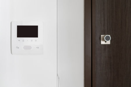 Close up view of surveillance monitor with electronic doorbell on white wall. Brown wooden door near intercom device with video connection and copy space display. Concept of smart home protectionの写真素材