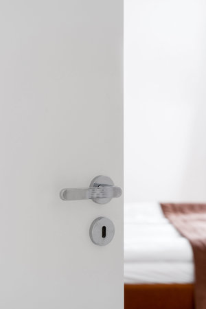 Vertical shot of opened white door to modern bedroom interior or hotel room. Metal handle and keyhole. Privacy and comfortable concept. Copy spaceの写真素材