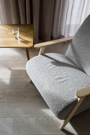 High angle view on empty and stylish armchair with grey upholstery standing near wooden table with glass of drinking water on top. Sophisticated modern apartment. Comfortable furniture in roomの写真素材