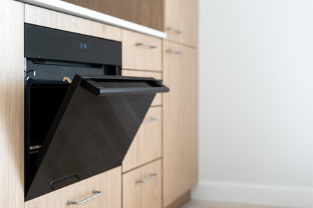 Selective focus on new oven with open door against white copy space background in kitchen. Side view of modern design of induction cooker in apartmentの写真素材