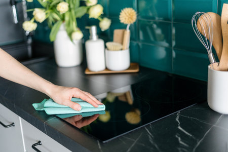 cropped shot of female hand with microfiber rag cleaning glass ceramic electrical hob on marble countertop in stylish kitchen, housework conceptの写真素材