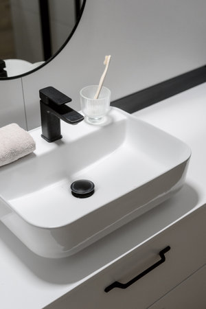 high angle shot on white ceramic washbasin with black mixer and glass with toothbrush in domestic washroom with luxury interior, morning routine conceptの写真素材