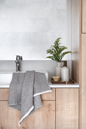 detail in bathroom interior, clean towel on washbowl, chrome mixer, soap in dispenser bottle, vase with plant and massage brush on wooden tray on countertopの写真素材