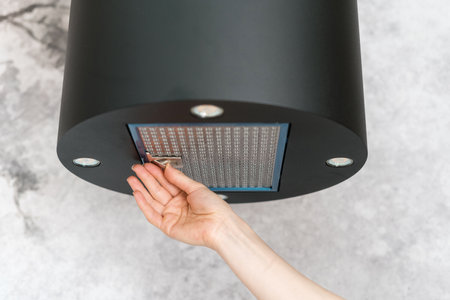 Woman removing filter from cooker hood for cleaning or service. Process of replacing dirty elements in kitchen extractor fan. Modern appliance for air purification during cooking food in apartmentの写真素材