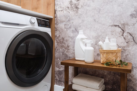 plastic bottles with laundry detergent on wooden shelf near automatic washing machine in domestic bathroom, advertising conceptの写真素材