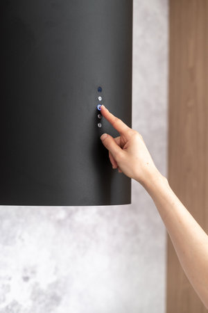Cropped shot of female hand press button and using black hood extractor while preparing food at home, modern household appliance conceptの写真素材