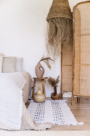 Boho style bedroom with decorative elements from natural materials, wooden dressing screen, ceramic vases and cotton rug. Side table with flowers near comfort bed. Cozy ethnic interior designの写真素材