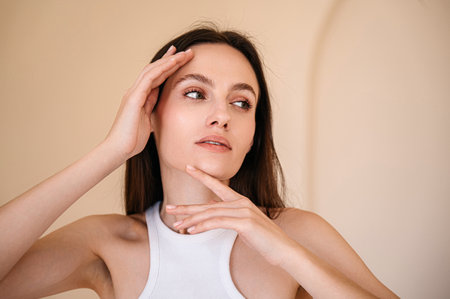 woman with healthy skin and natural makeup posing on camera, looking aside, touching her perfect face. beauty salon, eyebrow lamination procedure, skincare conceptの写真素材
