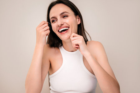 oral care for clean teeth and fresh breath. portrait of happy woman with wide smile brushing her teeth holding dental floss. model standing isolated on copy space backgroundの写真素材