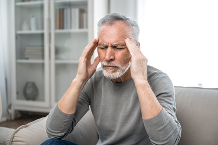 Portrait of tired unhealthy senior man massaging temples, suffering from terrible headache or migraine. Having high blood pressure. Stressed and exhausted life.の写真素材