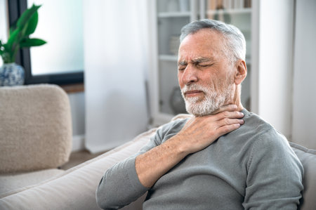 Mature aged man suffering from strong throat sore or angina. Concept of health problems, losing of voice, pain and itching. Elderly person feeling discomfort and difficulty to swallow.の写真素材
