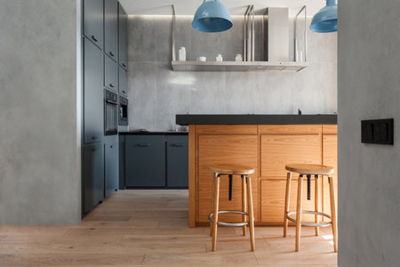 flat studio with stylish interior. kitchen island with dark countertop, wooden bar stools, cabinet furniture and modern household appliancesの写真素材