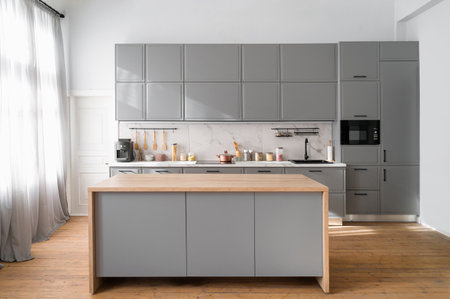 Bright minimalistic kitchen interior with gray furniture and big dining table on wooden floor. Cooking utensils and jars with food on countertop.の写真素材
