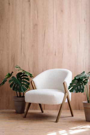 Vertical shot of white comfortable chair in room with wooden planks on wall. Green monstera, houseplants in pots close to soft furniture in lobby. Nordic style interior with hardwood floor. Copy spaceの写真素材