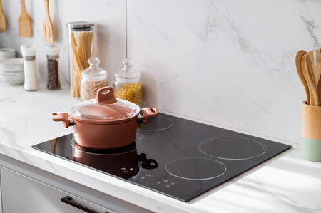 Clean new and black induction stove with control panel near marble countertop on white kitchen....