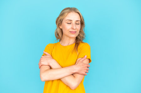 Portrait of dreamy woman hugging herself isolated over blue copy space background. Concept of self love, care and protect. Advertising on mental health support, healthcare and healthy lifestyleの写真素材