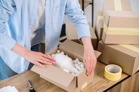 Cropped view of woman preparing parcel delivery for client. Entrepreneurs arranging fragile goods...