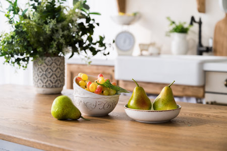 selective focus on ripe pears on plate, grape in ceramic bowl and flowers in vase on wooden dining table on home kitchen background. fresh fruits on tabletop. healthy eating concept.の写真素材