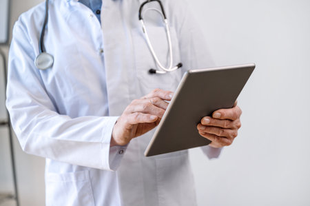 Cropped view of mature doctor holding modern digital tablet and using healthcare application in hospital for remotely communicate with patient. Prescription for medicine, online consultation conceptの写真素材