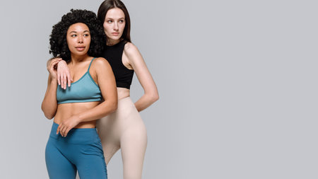 Portrait of sporty women rest after workout in gym, stand together isolated on gray copy space background, looking aside. Banner view of two female friends hug and support each other. Fitness conceptsの写真素材