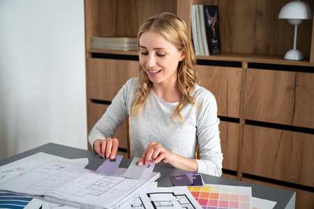 Creative people workplace. Interior designer working on new project, choosing color palette for painting walls at refurbish home. Smiling woman combine materials for renovated houseの写真素材