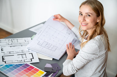 High angle view on young smiling female architect working with plans, documents, technical drawings,...