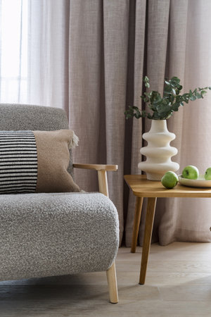 Soft grey couch or comfortable armchair standing near wooden table in light modern apartment. Design furniture and home decor in stylish and contemporary living room interiorの写真素材