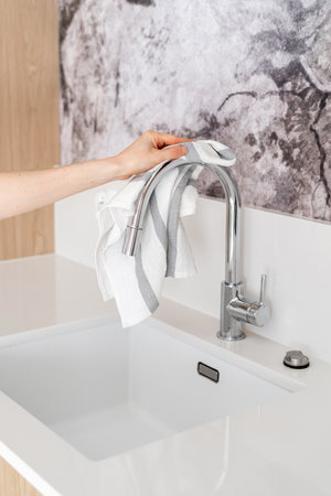 cropped shot of female hand hold cotton towel and wipe stainless steel faucet at modern kitchen, household chores conceptの写真素材