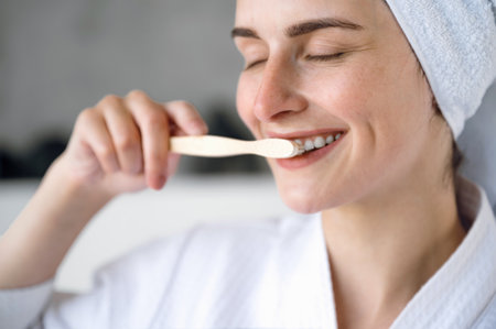 Healthcare, oral and dental care. Close up of smiling woman with closed eyes brushing white, straight teeth with wooden toothbrush. Female feeling satisfied from daily routine.の写真素材