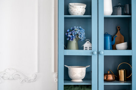 Blue vintage cupboard with kitchenware against white copy space wall. Shelves with home decor, clean plates, salad bowls and teapots. Convenient storage in provence style kitchen.の写真素材