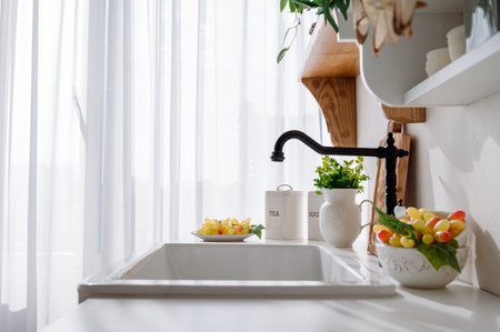 side view on kitchen sink and black faucet in vintage style. bowl with ripe grape, green fresh parsley in jug and metal food containers on white countertop in bright roomの写真素材